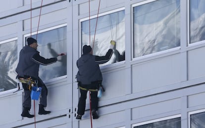 Unos trabajadores limpian los cristales de las ventanas de uno de los pabellones del parque Olímpico.