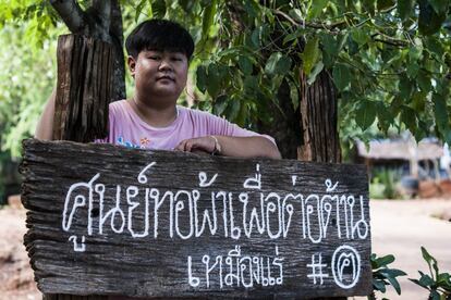 Wanpen Kunna, de 21 años, junto a la entrada del centro de Na Nong Bong. El cartel dice: "Centro para tejer contra la mina". Tungkum Limited presentó una denuncia por difamación criminal contra ella cuando tenía 15 años. Los cargos se referían a su intervención en un videoclip informativo en el que afirmaba que las aldeas y los recursos hídricos cercanos a la mina se habían visto afectados por el impacto de las actividades mineras.  Todos los cargos fueron desestimados en 2016.