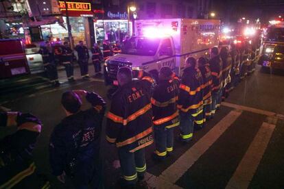 La ambulancia con los agentes asesinados pasa frente una guardia de honor de los bomberos.