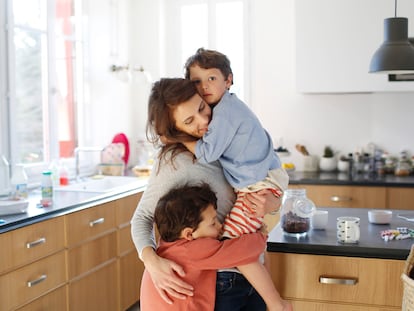 Una madre abraza con fuerza a sus hijos en la cocina.