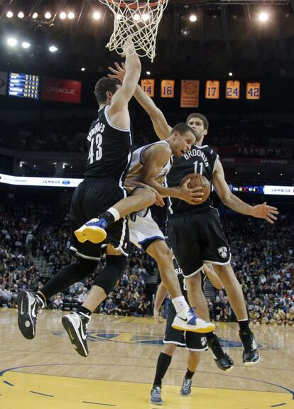 Stephen Curry, de los Golden State Warriors, intenta anotar ante Brook Lopez y Kris Humphries, de los Brooklyn Nets