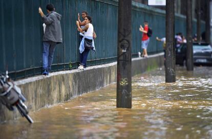 Pessoas tentam atravessar uma área alagada  no Rio. Ao menos quatro pessoas morreram em decorrência da chuva 