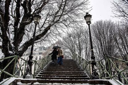 Dos jóvenes bajan la pasarela para cruzar el canal Saint-Martin mientras la nieve cae sobre la capital francesa.