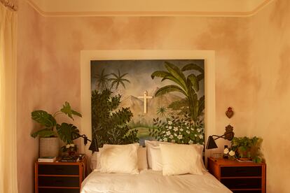 En el dormitorio principal, un paisaje tropical sirve de cabecero de la cama, flanqueada por mesillas vintage del Rastro, apliques de la serie PS de Ikea, imaginería religiosa y más plantas.