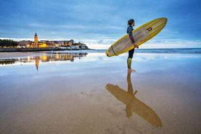 Una surfera en la playa de San Lorenzo, en Gijón, con la iglesia de San Pedro al fondo.