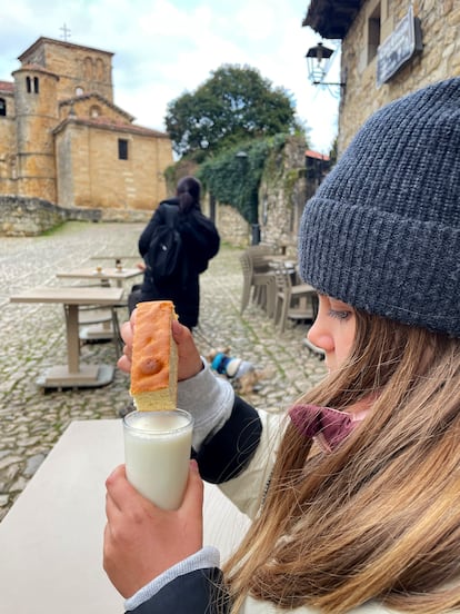 Una joven moja el bizcocho en el vaso de leche, en la puerta del establecimiento.