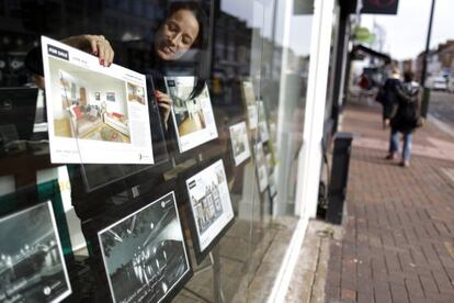 Una empleada coloca el cartel de 'Se vende' en el escaparate de una inmobiliaria en una calle londinense.