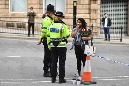 A police officers (L) talk with a woman carrying a bunch of flowers near the Manchester Arena in Manchester, northwest England on May 23, 2017 following a deadly terror attack at the concert at the venue the night before. 
Twenty two people have been killed and dozens injured in Britain's deadliest terror attack in over a decade after a suspected suicide bomber targeted fans leaving a concert of US singer Ariana Grande in Manchester. / AFP PHOTO / Ben STANSALL
