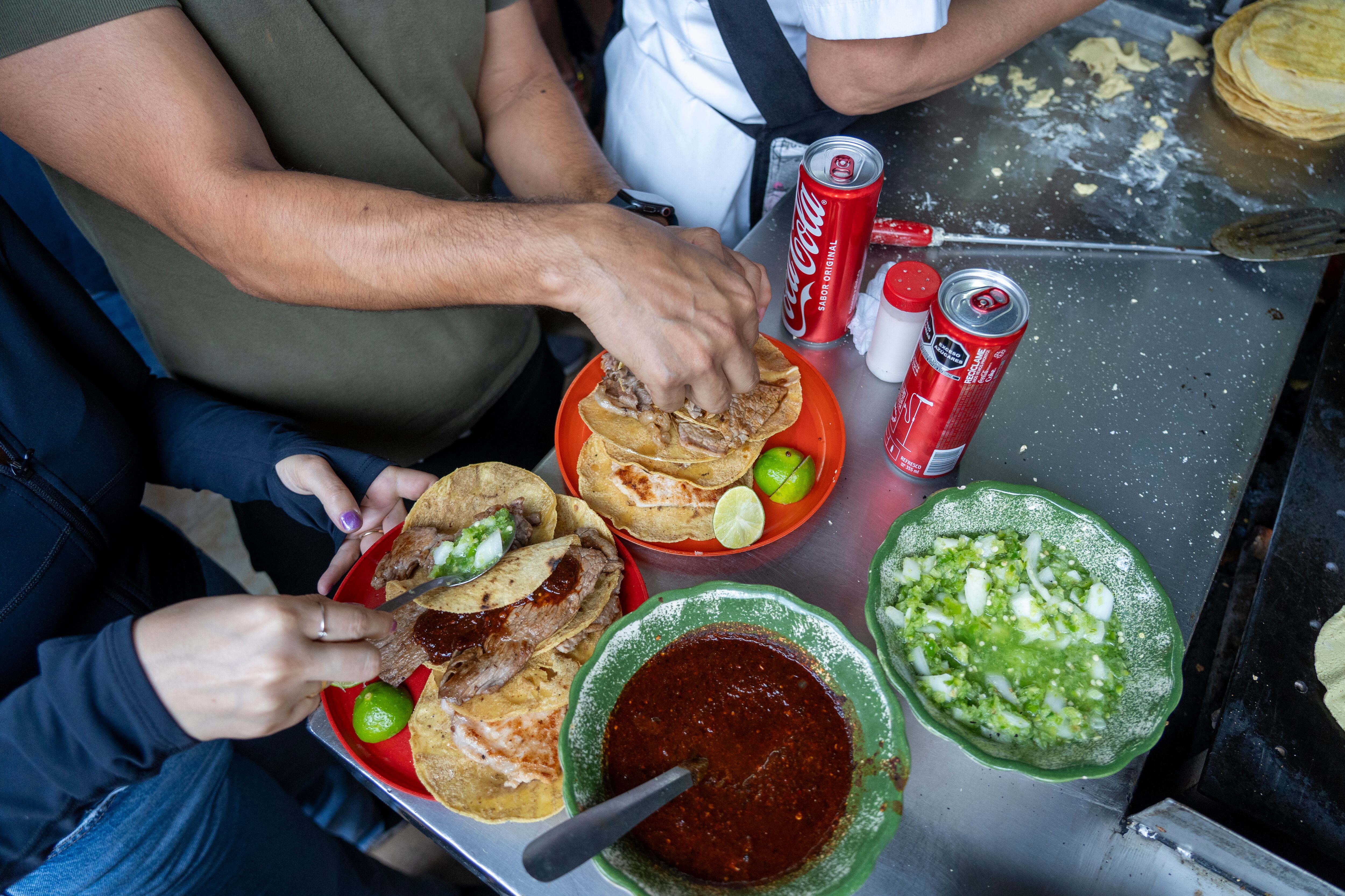 Comensales ponen salsas, cebolla y cilantro a sus tacos, este jueves.
