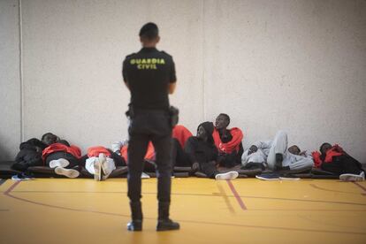 Un Guardia Civil frente a un grupo de migrantes trasladados a un polideportivo de Tarifa.