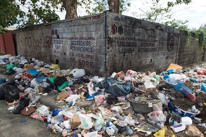 Basura en una acera de San Cristóbal junto a un muro en el que se lee 'No basura en esta sera'.