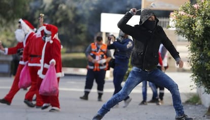 Un palestino lanza una piedra con una honda a soldados israel&iacute;es, con varios hombres vestidos de Santa Claus a su espalda, en Bel&eacute;n.
