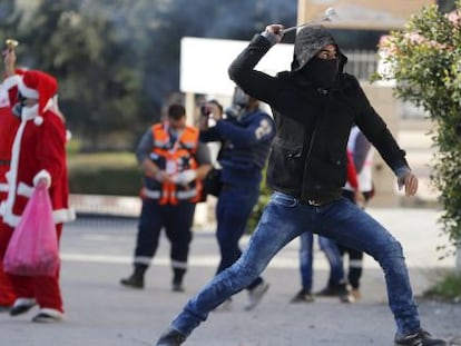 Un palestino lanza una piedra con una honda a soldados israel&iacute;es, con varios hombres vestidos de Santa Claus a su espalda, en Bel&eacute;n.