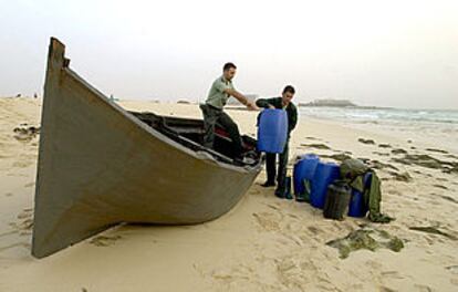 Dos guardias civiles descargan bidones de una patera que encalló anteayer en una playa de Fuerteventura.