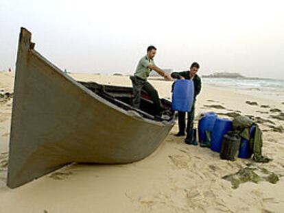 Dos guardias civiles descargan bidones de una patera que encalló anteayer en una playa de Fuerteventura.