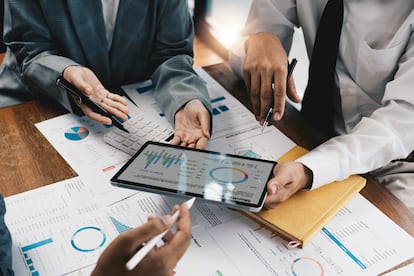 Close up business adviser partnership coworkers using a tablet to chart company financial statements report and profits work progress and planning in office room