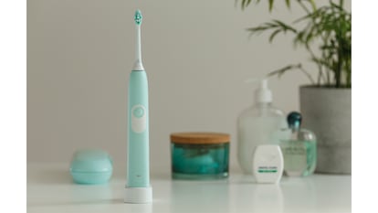 Un cepillo de dientes sobre un cargador inalámbrico en una imagen rodeado en segundo plano por otros elementos de higiene personal