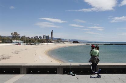 Una mujer y su hijo observan la playa desierta de la Nova Icária de Barcelona, esta mañana durante la salida permitida por el Gobierno a los menores de 14 años.