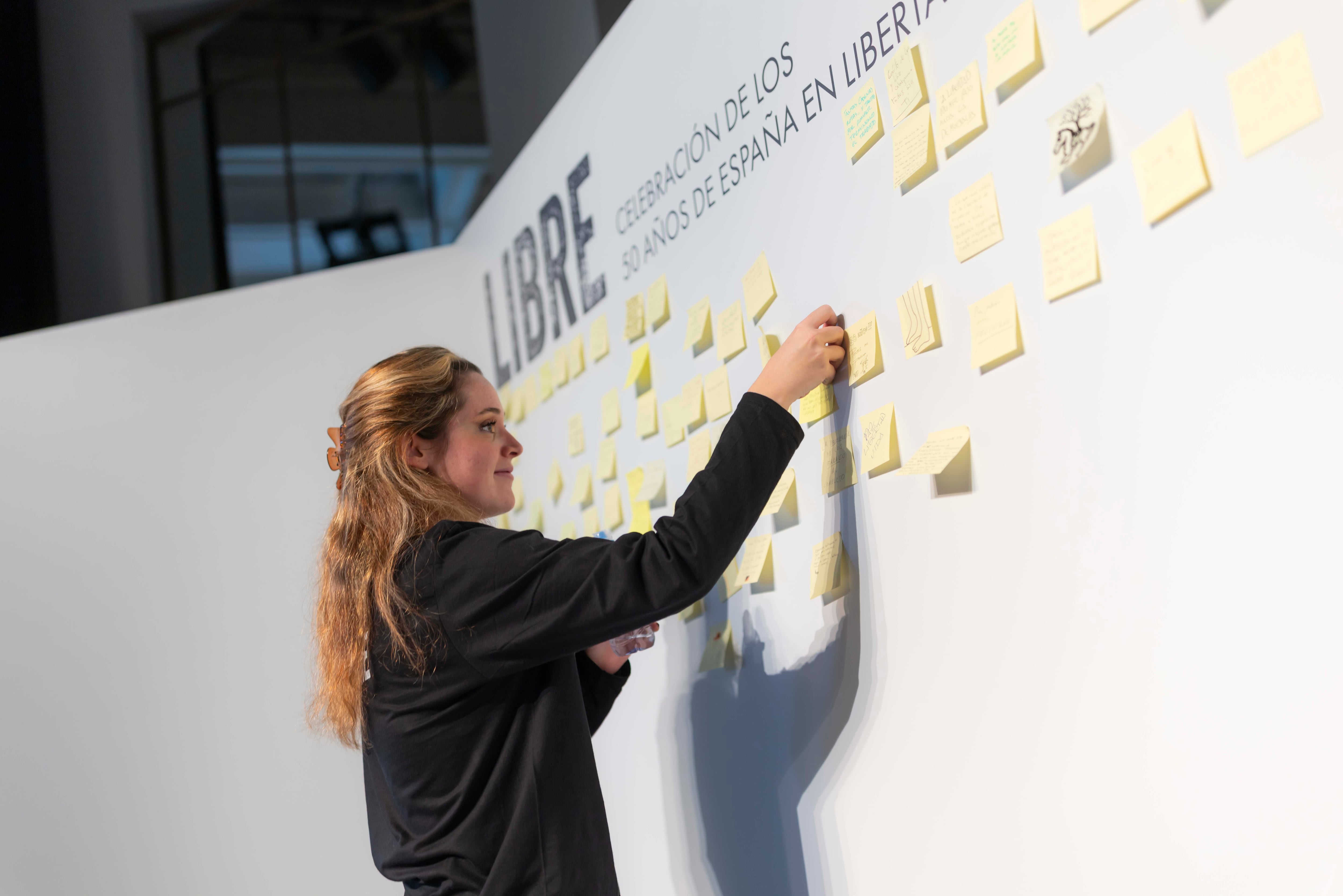 Una de las asistentes a la exposición pega en el mural una reflexión sobre el medio siglo de democracia en España.
