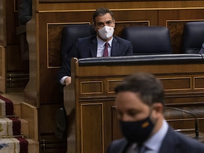 El presidente del Gobierno, Pedro Sánchez, sentado en su escaño, observa al líder de Vox, Santiago Abascal, en el Congreso.