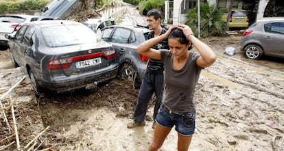 Dos vecinos de Vera (Almería) caminan entre lodo junto a varios vehículos arrastrados en las inundaciones.