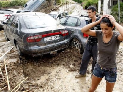 Dos vecinos de Vera (Almer&iacute;a) caminan entre lodo junto a varios veh&iacute;culos arrastrados en las inundaciones. 