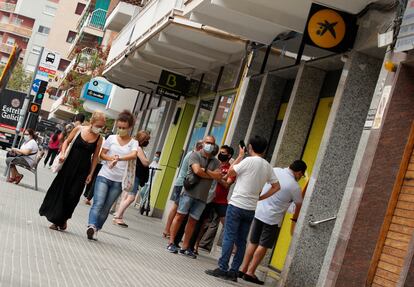 Varias personas esperan junto a oficinas de Caixabank y Bankia en Barcelona.