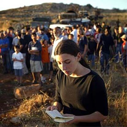 Una joven lee un libro de oraciones mientras un grupo de judíos bloquea al Ejército israelí el acceso al asentamiento de Ofra.