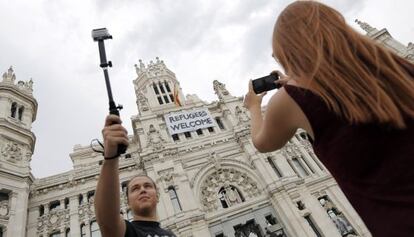 Dos jóvenes toman fotos del Ayuntamiento con la pancarta de apoyo a los refugiados.