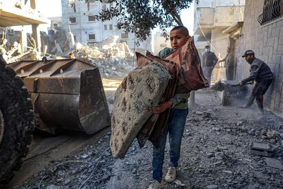 Un niño sujeta cojines y almohadas mientras un tractor limpia de escombros una calle en Rafah, este viernes. 