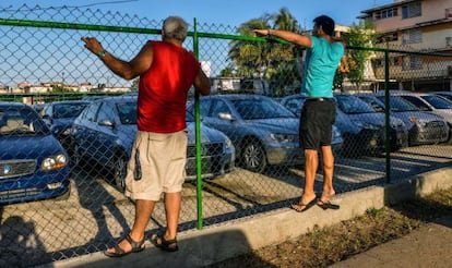 Cubanos observam um pátio com carros usados à venda.