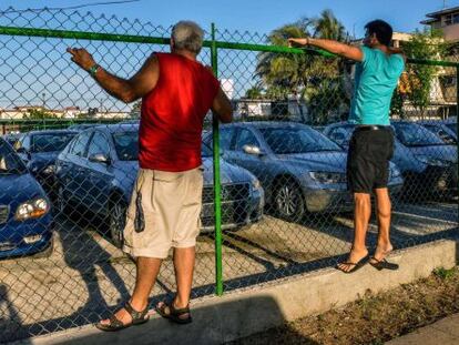 Cubanos observam um pátio com carros usados à venda.