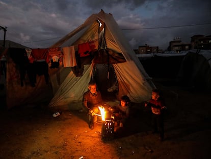 Un grupo de palestinos desplazados entra en calor frente a un fuego cerca de su tienda de campaña este martes en Rafah (sur de Gaza).