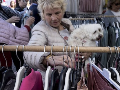 Una mujer ojea varias prendas con su perro en brazos en el mercadillo de Majadahonda.