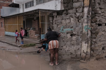 Priscila se aferra a un muro acribillado a balazos mientras ayuda a una de sus hijas a saltar un charco.