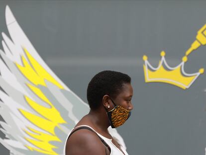 Una mujer con mascarilla pasea junto a un mural que muestra una jeringuilla, en Ciudad del Cabo, Sudáfrica.