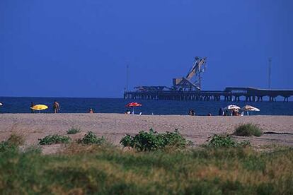 La playa del puerto de Sagunto, en la comarca valenciana de El Camp de Montvedre. Al fondo, pasarela industrial para el transporte de mercancías.