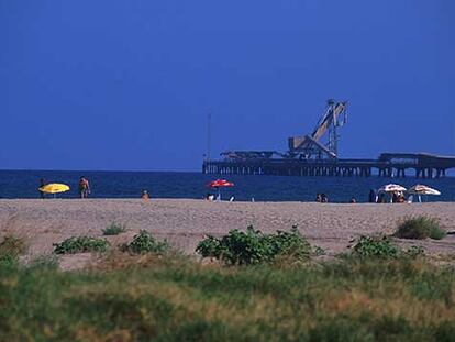 La playa del puerto de Sagunto, en la comarca valenciana de El Camp de Montvedre. Al fondo, pasarela industrial para el transporte de mercancías.