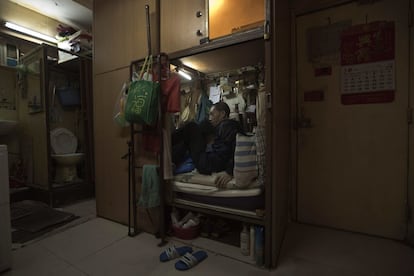 Wong Tat-ming en su casa ataúd, junto a un conjunto de inodoros sucios. Wong paga 310 dólares al mes por un compartimento que mide 91x182 cm. Está repleto de todas sus escasas posesiones, incluyendo un saco de dormir, un pequeño televisor en color y un ventilador eléctrico.