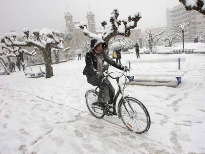 Una ciclista desafía a la nieve en los jardines de Alderdi Eder, con el Ayuntamiento donostiarra al fondo.