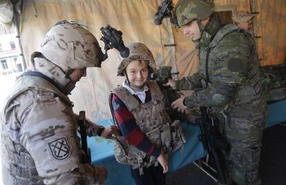 Dos soldados ayudan a un niño a vestirse en equipo de combate durante la jornada de puertas abiertas del Acuartelamiento de Loyola.