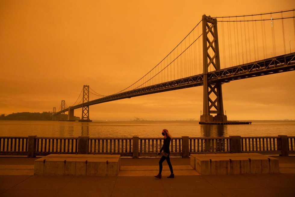 Una mujer camina por el embarcadero, en las cercanías del puente de la Bahía, bajo un cielo lleno de humo, en San Francisco.
