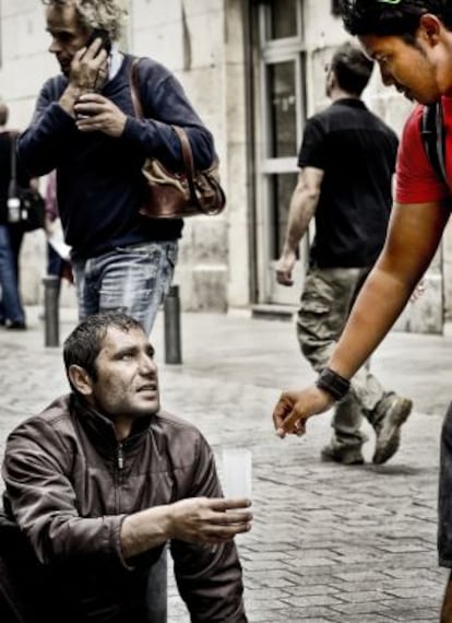 A passer-by gives a coin to a homeless man on the streets of Madrid.