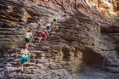 Cuatro millones y medio de personas visitan cada año el parque nacional del Gran Cañón, en Arizona, Estados Unidos. Los visitantes pueden asomarse al vacío desde la vertical de 1.300 metros del Skywalk, una pasarela de acero con suelo de cristal, o adentrarse en sus entrañas como los jóvenes de la foto, tomada en el North Canyon, una garganta con espectaculares escalones de arenisca. Este enclave forma parte de las rutas senderistas de las empresas de turismo activo de Salt Lake City, Phoenix o Flagstaff. La mayoría de los turistas que acceden por carretera lo hacen por la cornisa sur (South Rim), desde las ciudades de Williams o Flagstaff hasta Grand Canyon Village, la zona de servicios dentro del parque nacional. El Gran Cañón mide 446 kilómetros de este a oeste y ocupa 5.000 kilómetros cuadrados. En sus paredes se han identificado 40 estratos de rocas diferentes —las más antiguas, de 1.800 millones de años—, un registro que abarca tres de las cuatro eras geológicas de la Tierra.