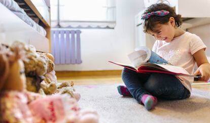 Una niña lee un libro ilustrado en su cuarto. 