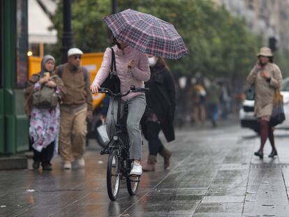 Una mujer en bici se protege con un paraguas, el pasado lunes en la avenida de la Constitución de Sevilla.