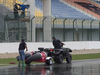 Unos comisarios tratan de quitar algo de agua de la pista con unas máquinas.