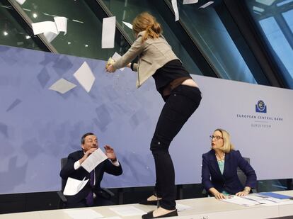 Una activista irrumpe en la rueda de prensa del presidente del Banco Central Europeo (BCE), Mario Draghi. La mujer salta sobre la mesa al grito de "acabemos con la dictadura del BCE" y lanza confeti y papeles.