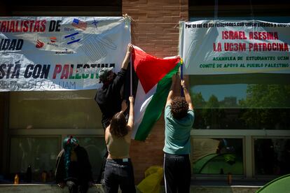 Tres jóvenes fijan un cartel a la fachada de La casa del estudiante, de la Universidad Complutense de Madrid, frente al campamento pro palestino.