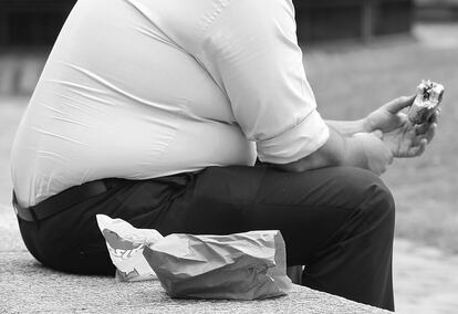 Un hombre con sobrepeso come comida rápida.